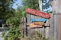 "A series of signs nailed to a wooden fence. They include the following: a red sign that reads Main Street, a blue arrow pointing right, and a pink sign that says Mayor Stubbs with an arrow pointing in the same direction. Mayor Stubbs is a cat that people like to say runs the town."