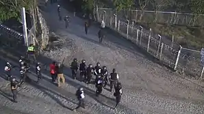 fifteen uniformed guards pointing guns at people moving away down road