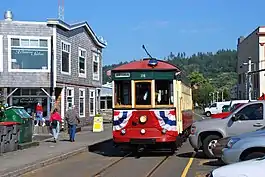 Red streetcar with creamy-white windowpanes on trolley tracks in narrow Astoria street, with green, forested hills in the background
