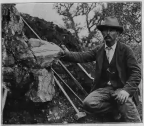 William E. Hidden next to a 73&nbsp;lb (33&nbsp;kg) mass of gadolinite in place at Barringer Hill, 1903.