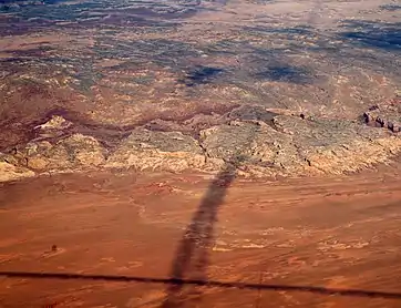 Shadows of contrails over San Rafael Reef —San Rafael Swell, Reef (perimeter), and San Rafael Desert at south & southeast. The Reef is most of the southeast, and east perimeter of the 45-mile-wide (72&nbsp;km) (west-to-east) San Rafael Swell, which trends southwest-by-northeast.