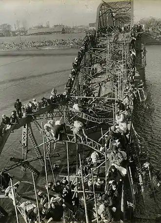 Black-and-white photo of people crossing a river via a destroyed bridge