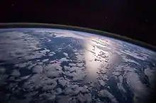 Image 39A view of Earth with different layers of its atmosphere visible: the troposphere with its clouds casting shadows, a band of stratospheric blue sky at the horizon, and a line of green airglow of the lower thermosphere around an altitude of 100&nbsp;km, at the edge of space (from Earth)