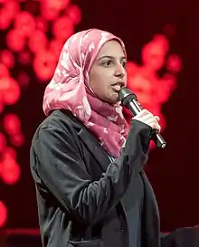 Girl wearing a pink hijab speaks into a microphone