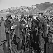 group of commandos with blackened faces drinking from cups. They have blankets around their shoulders and in the background are mountains