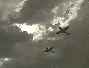 Two Spitfire single-seat piston-engined fighters in flight, silhouetted against cloud