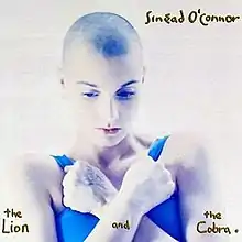 In a white background, Sinead O'Connor looking down while holding her arms in a crossed position.