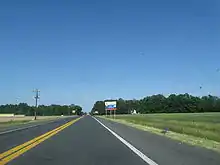 A two-lane road passing through farm fields. A blue and white sign on the right indicates an ongoing construction project on US&nbsp;113.